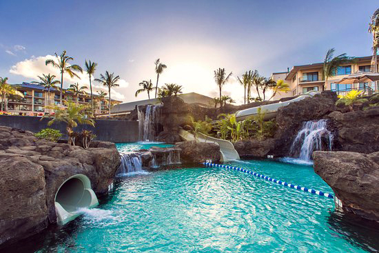 Resort-style pool with waterfall and tube slide at sunset
